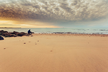 Caucasian man alone sitting on the shore of the sea, contemplating the sunset
