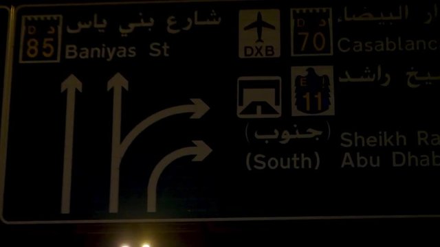 Moving towards the green road sign in the night street of the United Arab Emirates, travel concept. Stock. View from the windshield of a car on the traffic sign.