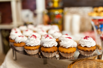 Delicious muffins with white cream on the wedding table for guests. Confectionery buffet with tasty muffins beautifully decorated on a nice stand. Close-up