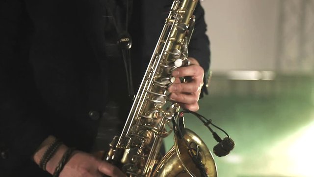 The artist plays the saxophone. Fingers press the keys of the saxophone