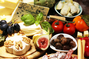 Italian antipasti wine snacks set. Cheese variety, Mediterranean olives, crudo, Prosciutto di Parma, salami and wine in glasses over grunge background.