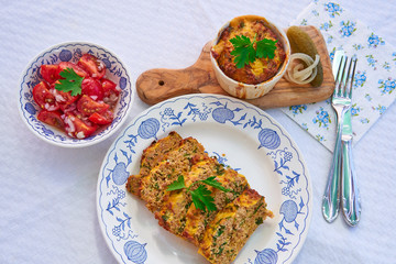 Top view on baked egg pie, kind of quiche, french style dish served on rustic plate with fresh tomato salad. Made from eggs, ham, parsley, pork and bread. Traditional spring food in Czech Republic.