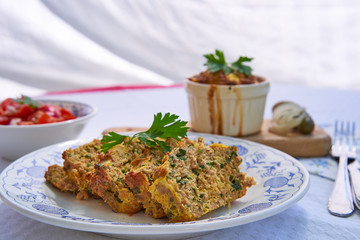 Baked egg pie or kind of quiche, french style dish served on rustic plate with fresh tomato salad. Made from eggs, smoked ham, parsley, pork meat and bread. Traditional spring food in Czech Republic.