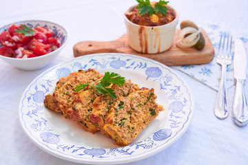 Close up Picture on the traditional baked czech spring dish, kind of salt cake or quiche, made from eggs, smoked ham, bread, pork meat and parsley, served on rustic plate with fresh tomato salad.