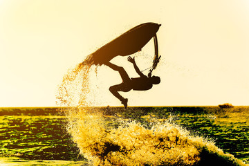 Silhouette of man drive freestyle jet ski at sunset.Professional rider do tricks in the sea,