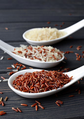Different types of rice in spoons on wooden table background