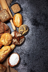 Assortment of baked bread and bread rolls on rustic grey bakery table background