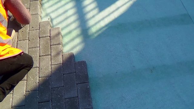 Construction worker laying interlocking paving concrete onto sheet nonwoven bedding sand and fitting them into place.