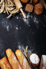 Assortment of baked bread and bread rolls on rustic black bakery table background