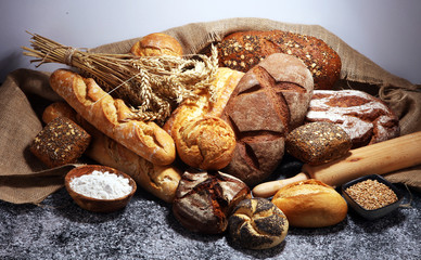 Assortment of baked bread and bread rolls on rustic grey bakery table background