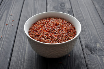 Red rice in a ceramic bowl against dark wooden background