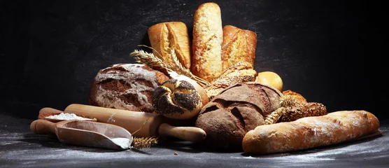 Foto auf Acrylglas Bäckerei Auswahl an gebackenem Brot und Brötchen auf rustikalem schwarzem Backtischhintergrund