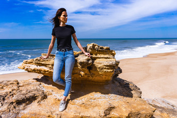 Young woman standing on cliff on beach in Nazare on Atlantic coast