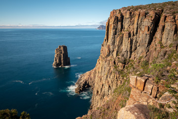 Steep brown-orange cliffs near Cape Hauy in blue sea, Tasmania Australia