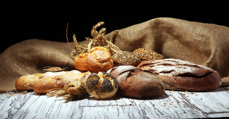 Assortment of baked bread and bread rolls on rustic white bakery table background