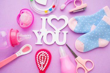 Newborn baby story. Strow heart and children's toys, scissors, baby bottle, nipple, hairbrush on violet background