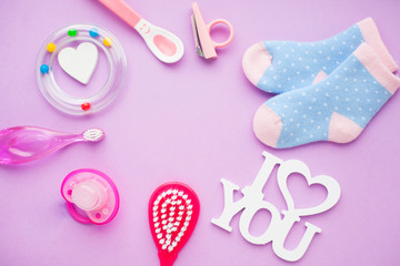 Newborn baby story. Strow heart and children's toys, scissors, baby bottle, nipple, hairbrush on violet background