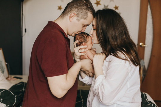parents kiss their newborn baby holding it in their arms