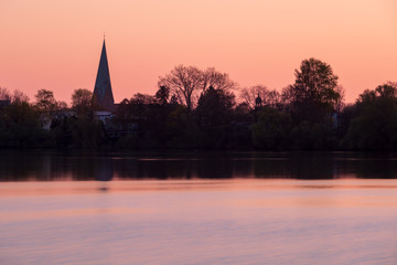 Fototapeta na wymiar Silhouette der Stadt Eutin am Sonnenaufgang über kleinem See mit Turm der Michaelis-Kirche, Schleswig-Holstein