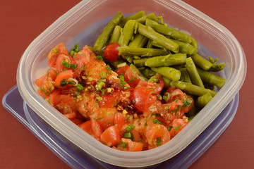 Baked salmon fish fillet with grape tomatoes and asparagus leftovers packed in plastic container for healthy work lunch