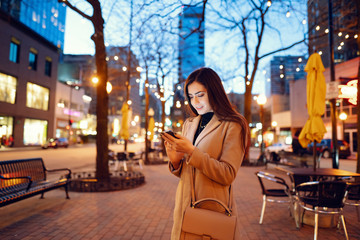 Beautiful girl in a evening city. Stylish brunette in a brown coat. Woman in a Chicago. Lady with a phone