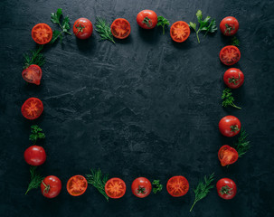 Composition of red tomatoes and green fresh parsley and dill lying on dark background in form of frame. Vegeterian food concept. Free space in middle