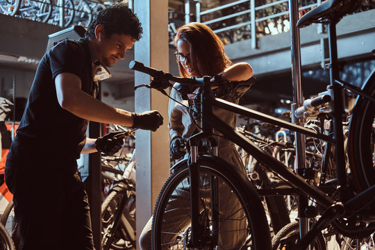 Young master and his attractive apprentice are fixing customer's bicycle at workshop.