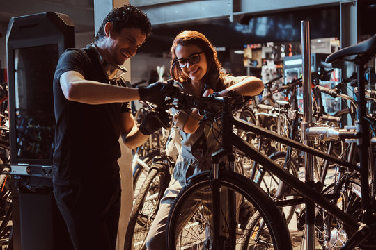 Young master and his attractive apprentice are fixing customer's bicycle at workshop. - Powered by Adobe