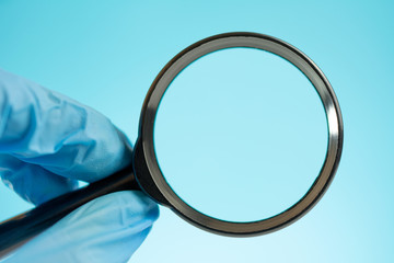 in the hands of a scientist a magnifying glass, blue medical gloves on a blue background close-up