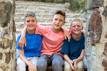 Three brothers sit together for a portrait by a stone wall