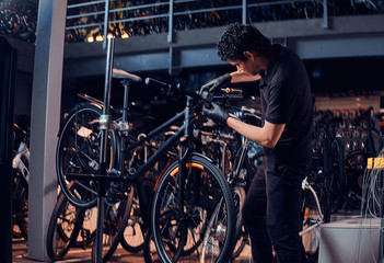 Diligent young mechanic is repairing customer's bicycle at workplace.