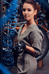 Fototapeta na wymiar Diligent beautiful girl is repairing bicycle at busy workshop between pneumatic wires.
