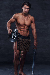 Fototapeta na wymiar Muscular man with sword and helmet is lookig to the camera. He is wearing gladiator's bandage.