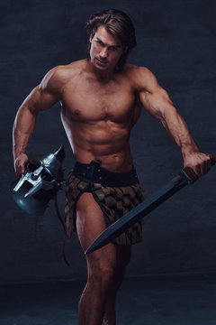 Muscular man with sword and helmet is lookig to the camera. He is wearing gladiator's bandage.