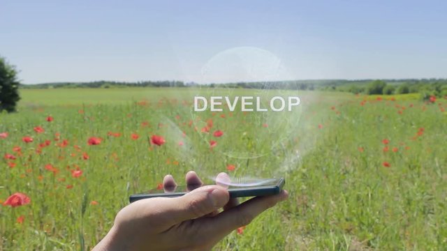 Hologram of Develop on a smartphone. Person activates holographic image on the phone screen on the field with blooming poppies