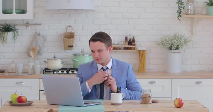 Morning coffee. Portrait of a young businessman with a cup of coffee in the kitchen behind a laptop