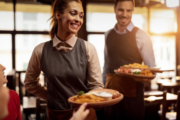 Happy waiters serving food to their guests in a restaurant.