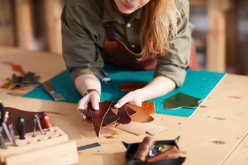 Warm toned close up of young  artisan holding leather pieces  in shoemaking  workshop, copy space - obrazy, fototapety, plakaty