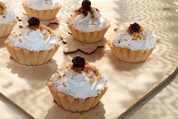 Cupcakes with cream close-up on wooden background. Selective focus. Tasty muffins sprinkled with powdered sugar in paper cups