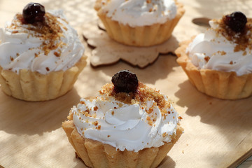 Cupcakes with cream close-up on wooden background. Selective focus. Tasty muffins sprinkled with powdered sugar in paper cups