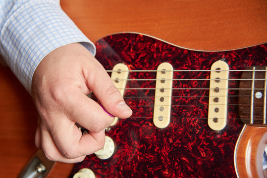 A man plays the electric guitar with a mediator