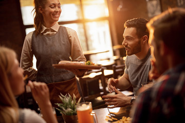 Happy waitress serving lunch to group of friends in a pub.