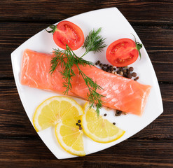 .red fish with lemon and tomatoes on a white plate