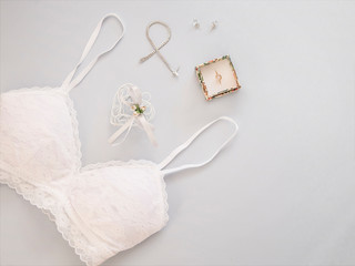 Obraz na płótnie Canvas Minimal flat lay with wedding accessories on light background. Sale wedding lingerie concept. Invitation template for celebration. Bride kit with bracelet, ring and white bra.