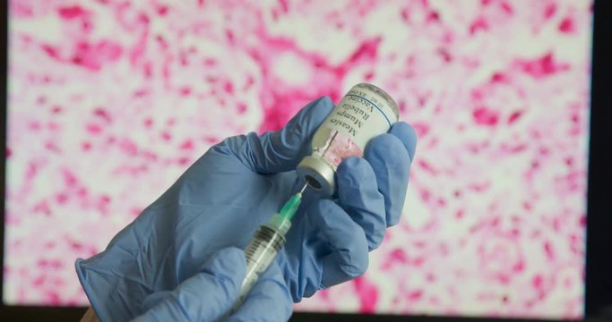 A medical professional fills a syringe with the measles vaccine with the virus displayed on a monitor in the background.