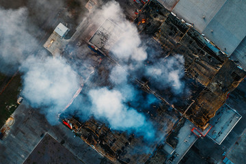 Top down view of smoke clouds from burnt warehouse building with burned roof, fire disaster accident in cargo logistics storehouse, aerial view