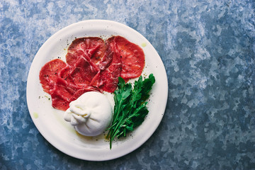 Delicious raw beef carpaccio with mozzarella, arugula and olive oil in a plate with spices top view space for text
