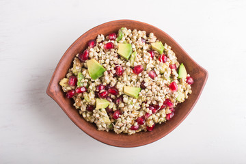 Salad of germinated buckwheat, avocado, walnut and pomegranate seeds in clay plate on white wooden background.