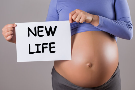 Image of close up stomach of pregnant woman holding paper with text new life on gray background.