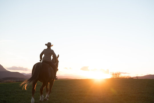 Man and woman riding horses against sunset sky on ranch